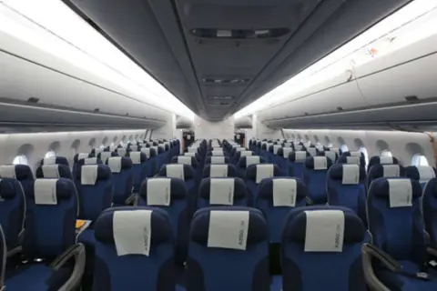 Reihe von blauen Flugzeugsitzen mit weißen Kopfstützen. Ein Sitzplatz D ist in der Mitte des Bildes zu sehen.