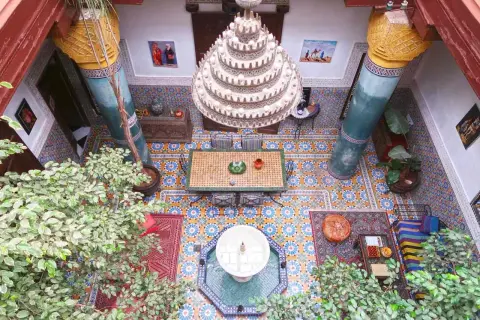 Ein Innenhof in Marrakesch mit Mosaikböden, einer Fontäne, üppiger Vegetation und einem Kronleuchter. Perfekt für einen entspannten Urlaub.