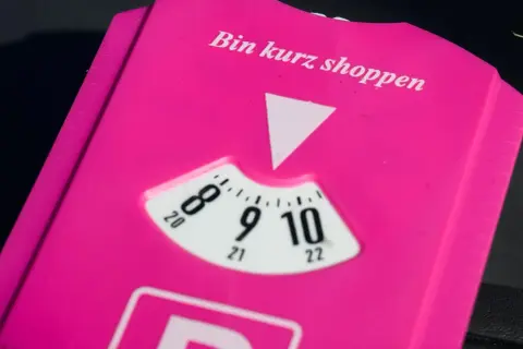 Pink parkschein mit der Aufschrift "Bin kurz shoppen". Die Parkscheibe ist auf 9 Uhr eingestellt.