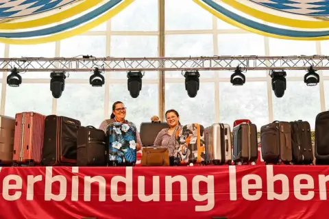 Zwei Frauen präsentieren eine Auswahl an Koffern für eine Auktion. Die Koffer sind in verschiedenen Farben und Mustern erhältlich.