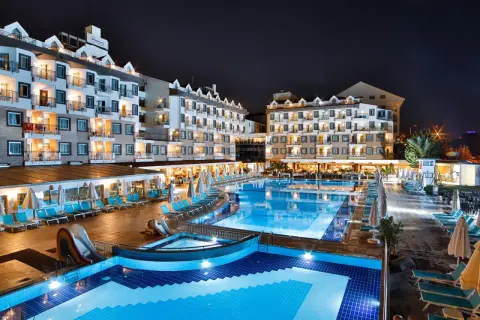 Nachtansicht des Diamond Beach Hotel & Spa mit beleuchteten Pools, Rutschen und Liegestühlen.