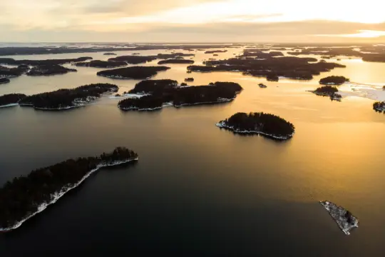 Winterliche Inselwelt im Sonnenuntergang. Dieses Bild könnte zeigen, welches Land die meisten Inseln hat, mit unzähligen kleinen Eilanden, die im goldenen Licht versinken.