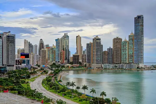 Moderne Skyline von Panama City mit hohen Wolkenkratzern, einer Küstenstraße und üppiger Vegetation am Wasser.