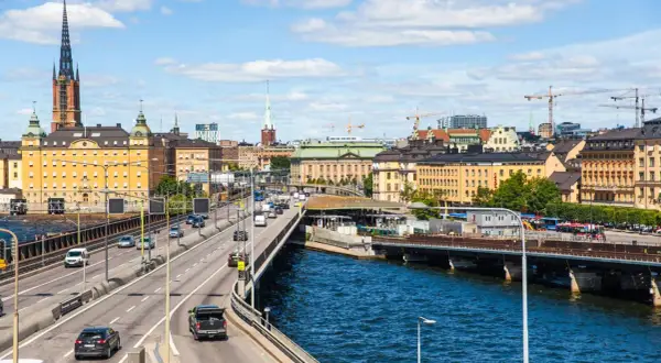 Blick auf die Skyline von Stockholm mit einem Fluss und einer Autobahn, auf der Autos fahren. Das Parken in Stockholm ist hier gut zu sehen.