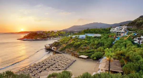 Sonnenuntergang am Club Marvy: Ein Strand mit vielen Liegen, ein Wasserpark und üppige Vegetation.