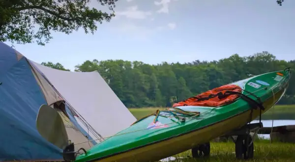 Grünes Kajak mit Schwimmweste auf einem Anhänger neben einem Zelt. Perfekte zelt gadgets für ein Abenteuer am See.