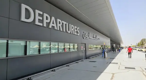 Große "DEPARTURES" Schriftzüge am Flughafen Dubai Terminal 3. Menschen und Autos spiegeln sich in den Fenstern.