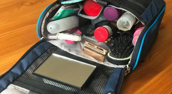 Offener Kulturbeutel mit Kosmetikartikeln: Zahnbürste, Rasierer, Kamm, Spiegel und diverse Fläschchen. Perfekte Packliste für unterwegs.