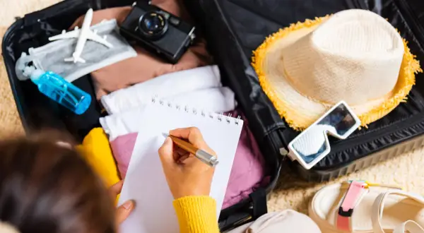 Packliste Portugal: Koffer packen mit Kleidung, Hut, Sonnenbrille, Kamera und Notizbuch.