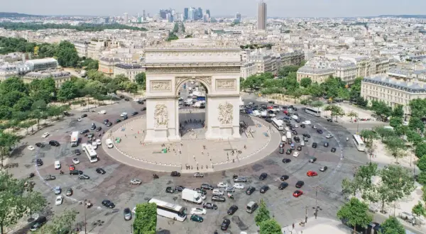 Ein Auto fährt durch Paris, vorbei am Triumphbogen. Die Skyline von Frankfurt ist in der Ferne zu sehen.