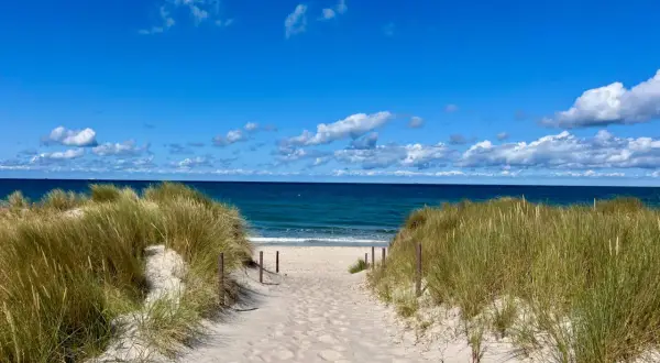 Sandiger Weg durch Dünen zum blauen Meer. Perfekter Urlaub am Meer mit Sonnenschein und Wolken.