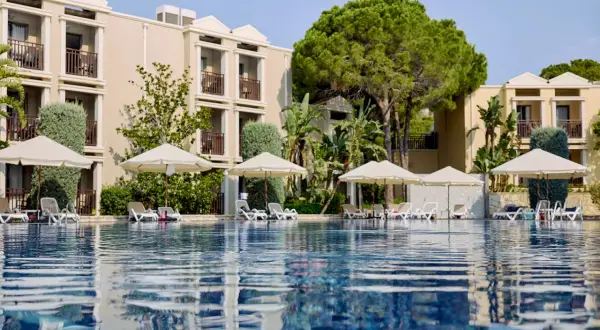 Ein Pool mit Liegen und Sonnenschirmen vor einem Hotelgebäude. Hier beginnt das magic life Belek.
