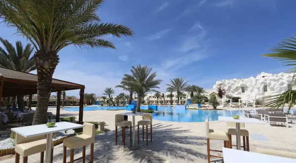 Sonnige Poolanlage mit Palmen und weißen Liegestühlen im Robinson Club Djerba.