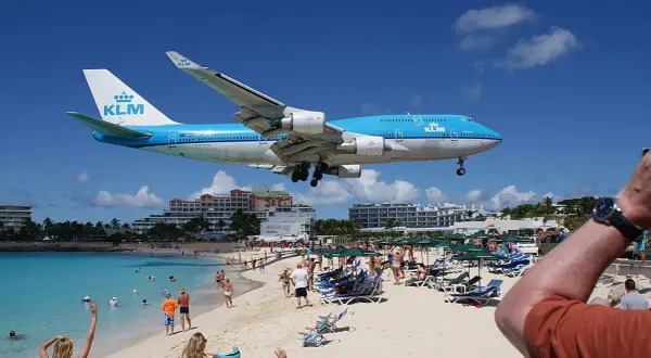 Ein KLM-Flugzeug landet tief über dem Maho Beach Flughafen. Urlauber am Strand winken dem Jumbo-Jet zu.