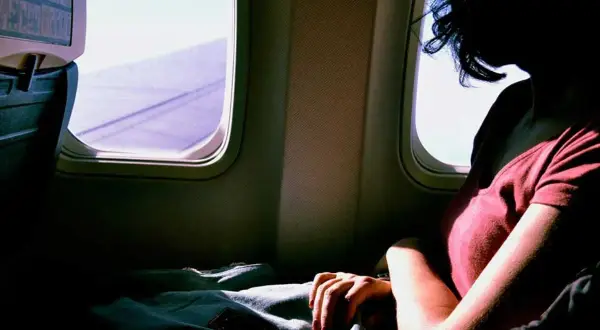 Frau mit extremer Flugangst blickt aus dem Flugzeugfenster. Die Flügel sind im violetten Licht zu sehen.