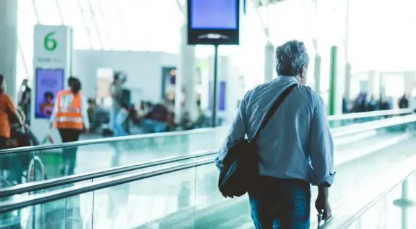 Mann mit Tasche auf Rolltreppe am Flughafen Frankfurt, auf dem Weg zum Geldwechsel.