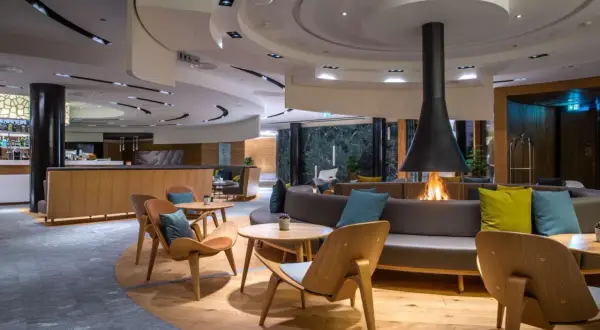 Gemütliche Lounge mit Kaminfeuer im Radisson Blu Hotel Andermatt. Moderne Sitzmöbel und Holzakzente laden zum Verweilen ein.