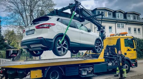 Ein weißer Nissan wird von einem Abschleppwagen in Frankfurt auf die Ladefläche gehoben. Die Abschleppkosten sind hier wohl im Service enthalten.