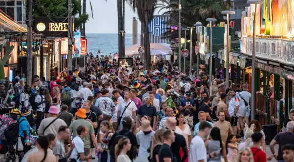 Volle Promenade auf Mallorca, viele Menschen unterwegs. Die Tourismussteuer auf Mallorca wird diskutiert, während Urlauber das Nachtleben genießen.