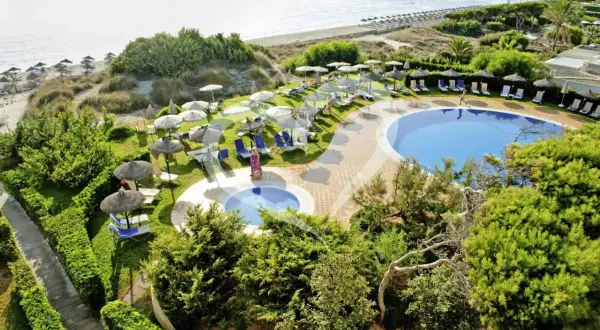 Einladende Pools und Liegen am Strand des Grupotel Natura Playa. Sonnenschirme spenden Schatten.
