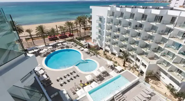 Ein modernes Hotel mit Pools und Liegestühlen, daneben ein Strand mit Palmen und dem Meer. Ein tropischer Traum!