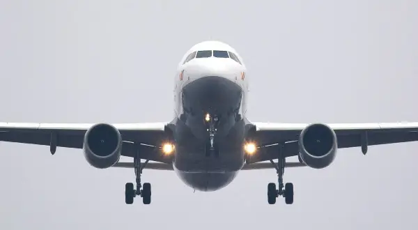 Ein Flugzeug nähert sich mit hoher Geschwindigkeit der Landebahn. Die Lichter am Fahrwerk leuchten hell.