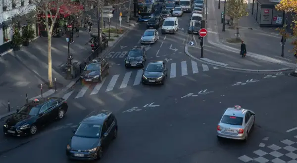 Verkehr in Paris: Autos und Taxis auf dem Weg zum Ziel. Ein silbernes Taxi fährt über den Zebrastreifen, während andere Fahrzeuge im Stau stehen.