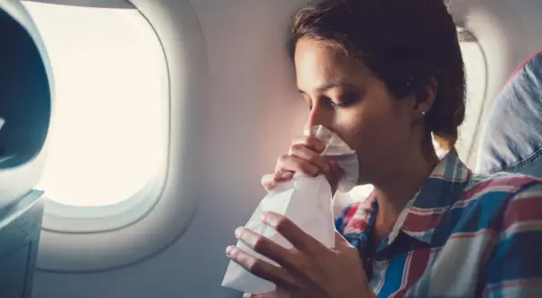 Frau mit Tüte gegen Reisekrankheit im Flugzeug.