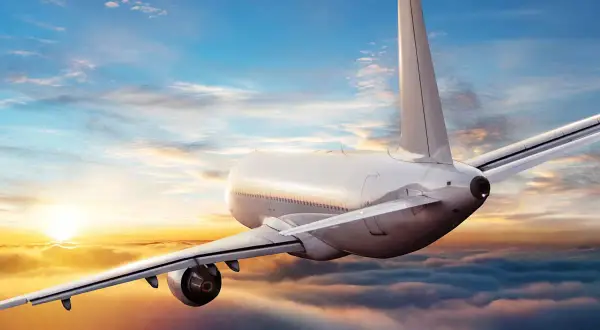 Ein Flugzeug fliegt über Wolken bei Sonnenuntergang. Die Frage, wie sicher ist fliegen aktuell, wird durch diese friedliche Szene beantwortet.