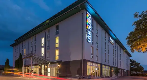 Das Park Inn Wien bei Nacht, beleuchtet mit bunten Lichtern. Autos fahren vorbei und hinterlassen rote Lichtspuren.