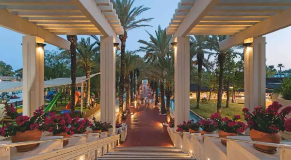 Ein beleuchteter Weg mit Palmen führt zum Seven Seas Hotel. Blumenkästen säumen die Treppe.