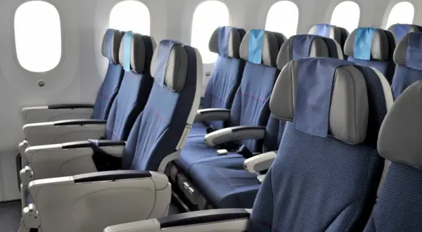 Reihe von blauen Flugzeugsitzen mit Kopfstützen und Armlehnen, daneben Fenster. Ein Fensterplatz im Flugzeug bietet Aussicht.