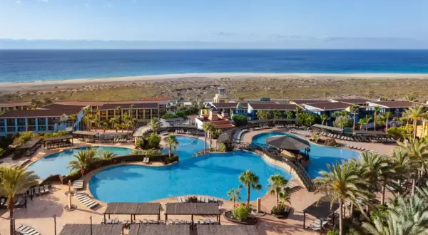 Ein Urlaubsparadies am Meer: Große Poollandschaft mit Palmen und Liegen, dahinter das Robinson Jandia Playa Resort und der weite Sandstrand.