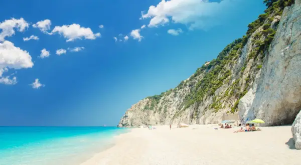 Traumhafter **Griechenland Sandstrand** mit türkisblauem Meer, weißen Klippen und einigen Sonnenanbetern.
