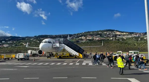 Passagiere steigen am Madeira Flughafen aus dem Flugzeug. Im Hintergrund erstreckt sich eine hügelige Landschaft mit Häusern.