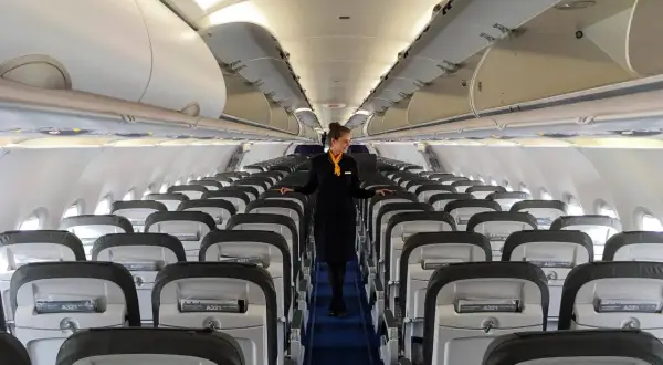 Flugbegleiterin in einem leeren Flugzeug. Die Reihen von Sitzen und die sorgfältige Präsentation lassen die Frage "Ist Lufthansa sicher?" positiv beantworten.