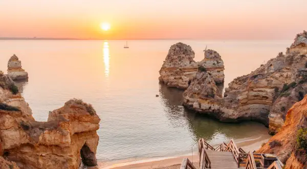 Sonnenuntergang an der Algarve: Ein perfekter Urlaub in Portugal am Meer mit Felsformationen und einer Holztreppe zum Strand.
