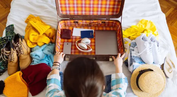 Packliste Mallorca: Koffer wird mit Kleidung, Schuhen, Kopfhörern, Reisepass und Laptop gepackt.