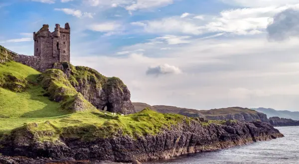 Ruinen einer Burg auf einem grünen Hügel über dem Meer. Schafe grasen friedlich. Was sollte man in Schottland nicht tun? Nicht hierher reisen!