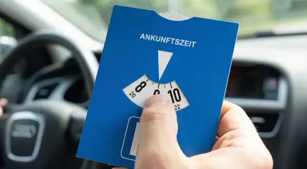 Blaue Parkscheibe mit Ankunftszeit-Einstellung im Auto. Beachten Sie die Regeln zum Parken mit Parkscheibe nach 18 Uhr.