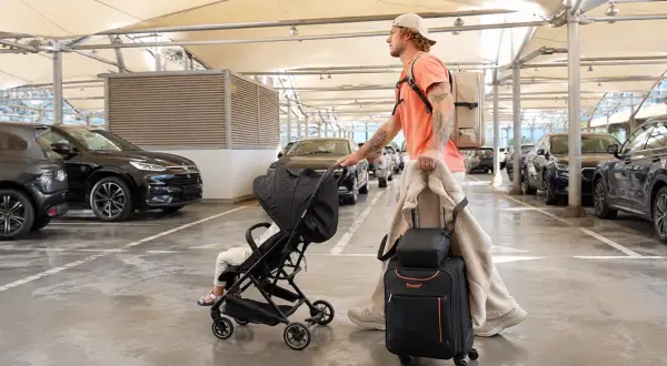 Mann mit Gepäck und Kinderwagen auf dem Parkplatz eines Flughafens.
