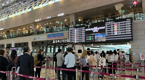 Menschen stehen in einer Schlange am Flughafen Seoul vor einer Anzeigetafel mit Abflugzeiten.
