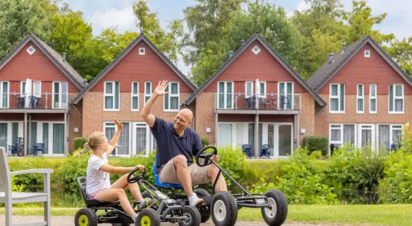 Vater und Tochter winken fröhlich, während sie mit Go-Karts durch die Anlage des TUI Kids Club fahren.