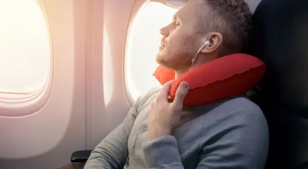 Mann schläft im Flugzeug mit rotem Nackenkissen. Ein Nackenkissen Flugzeug ist sinnvoll für bequemen Schlaf.