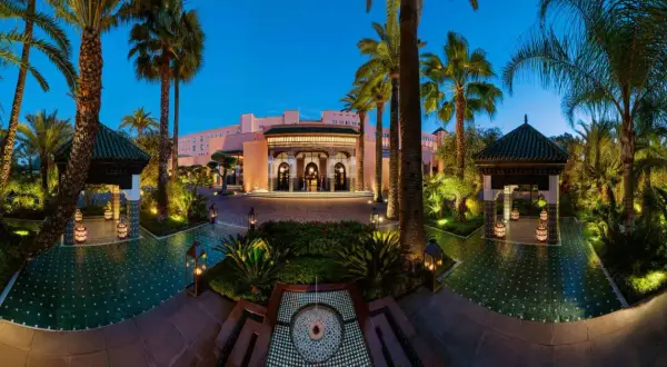 Eingangsbereich des La Mamounia Hotels in Marrakesch bei Dämmerung, umgeben von Palmen und beleuchteten Pavillons.