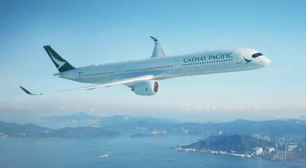Cathay Pacific Sicherheit: Ein modernes Flugzeug fliegt über einer Stadt und dem Meer.