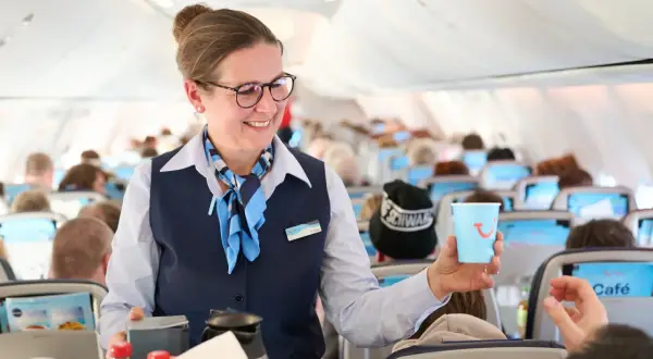 Flugbegleiterin von TUI fly bietet Kaffee an. Ein Lächeln und ein Getränk für die Passagiere.