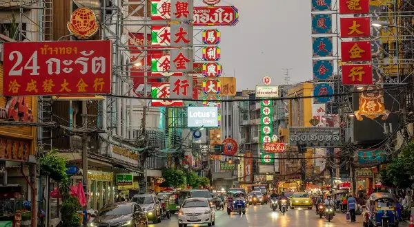 Bunte Neonschilder und Verkehr in Bangkok. Ein lebendiges Bild, das die pulsierende Atmosphäre und die einzigartigen Bangkok Erfahrungen widerspiegelt.
