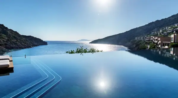 Infinity-Pool mit Blick auf die Bucht von Daios. Sonnenschein spiegelt sich im Wasser, Häuser schmiegen sich an den Hang.