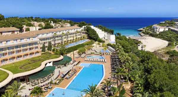 Blick auf das TUI Kids Club Cala Mandia Resort mit Pools, Strand und Meer.